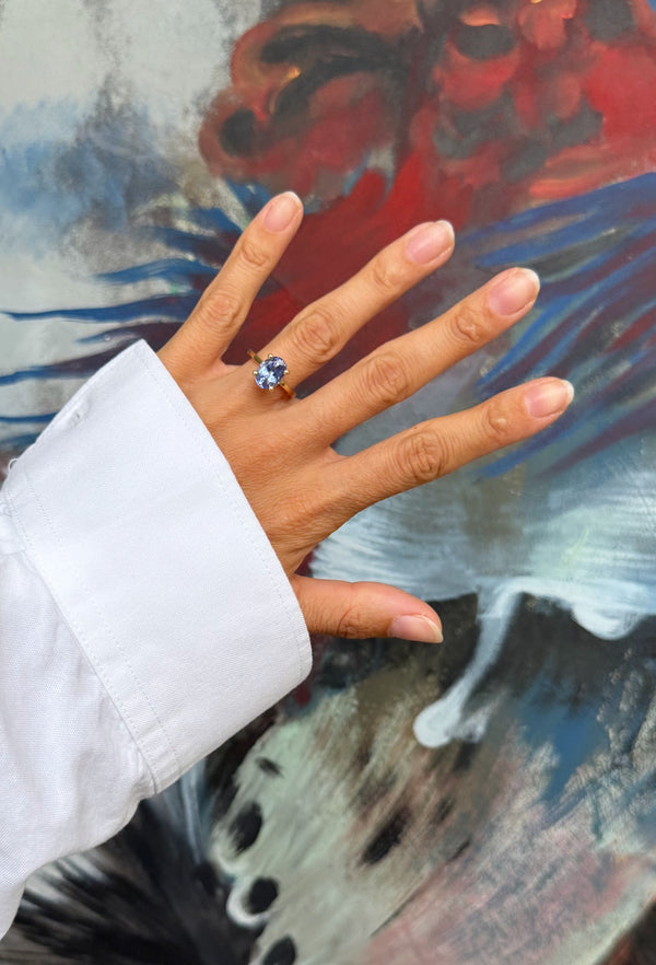Hand wearing a ring with a blue tanzanite gemstone against a colorful abstract painting background