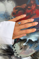 Hand wearing a ring with a blue tanzanite gemstone against a colorful background
